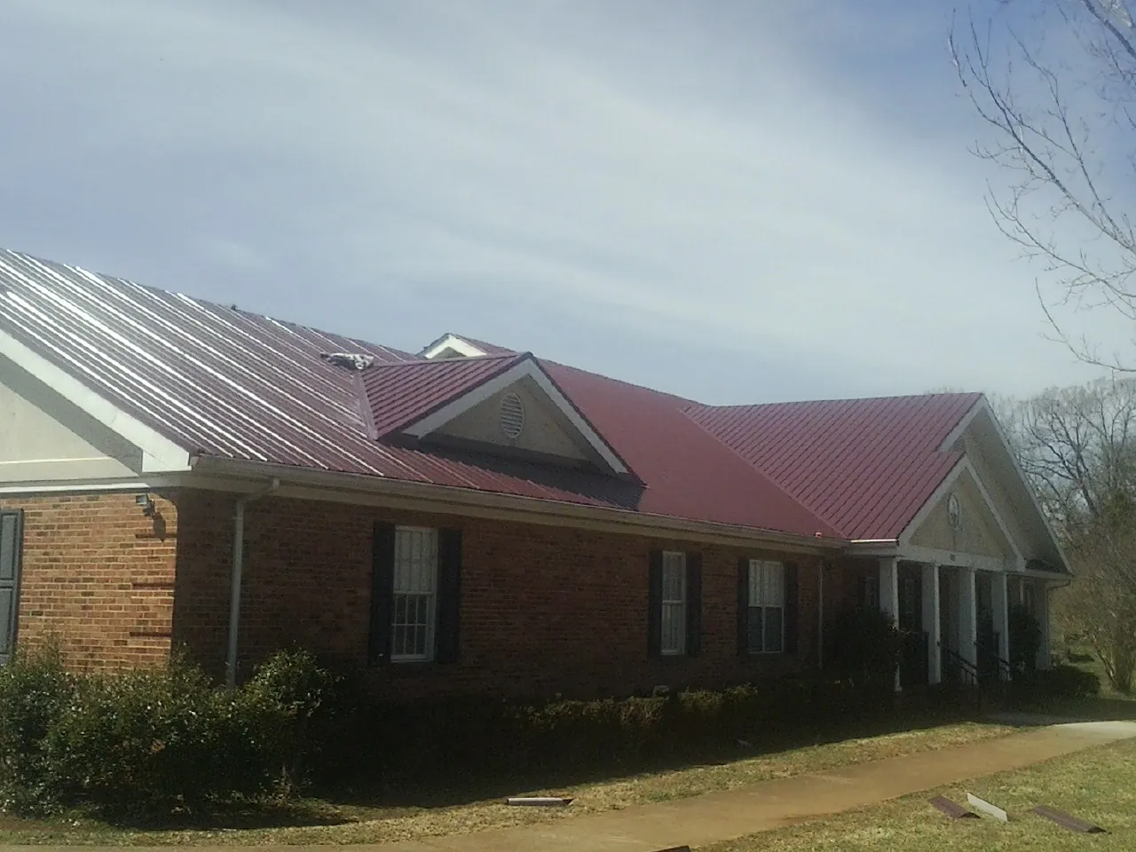 Red metal roof with gabled entries on a long brick building, from a Hail Damage Roof Repair job in Vanderbilt