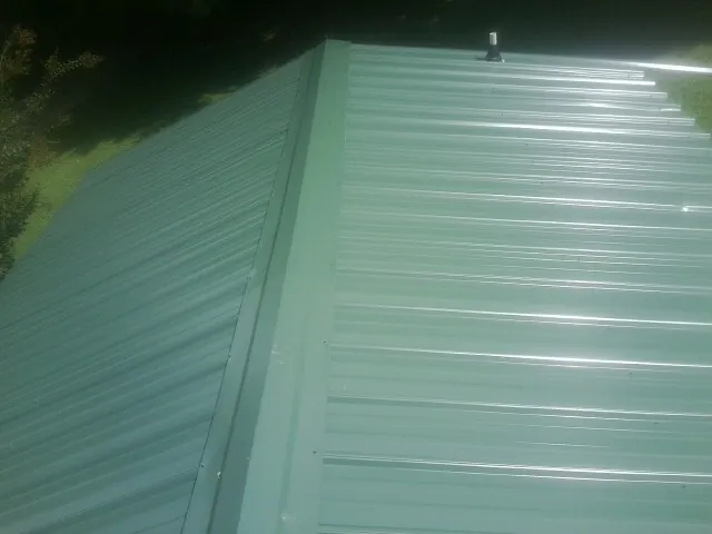 New green metal panels meeting at the ridge of a roof — Flat Roof Repair work by our crew in Vanderbilt