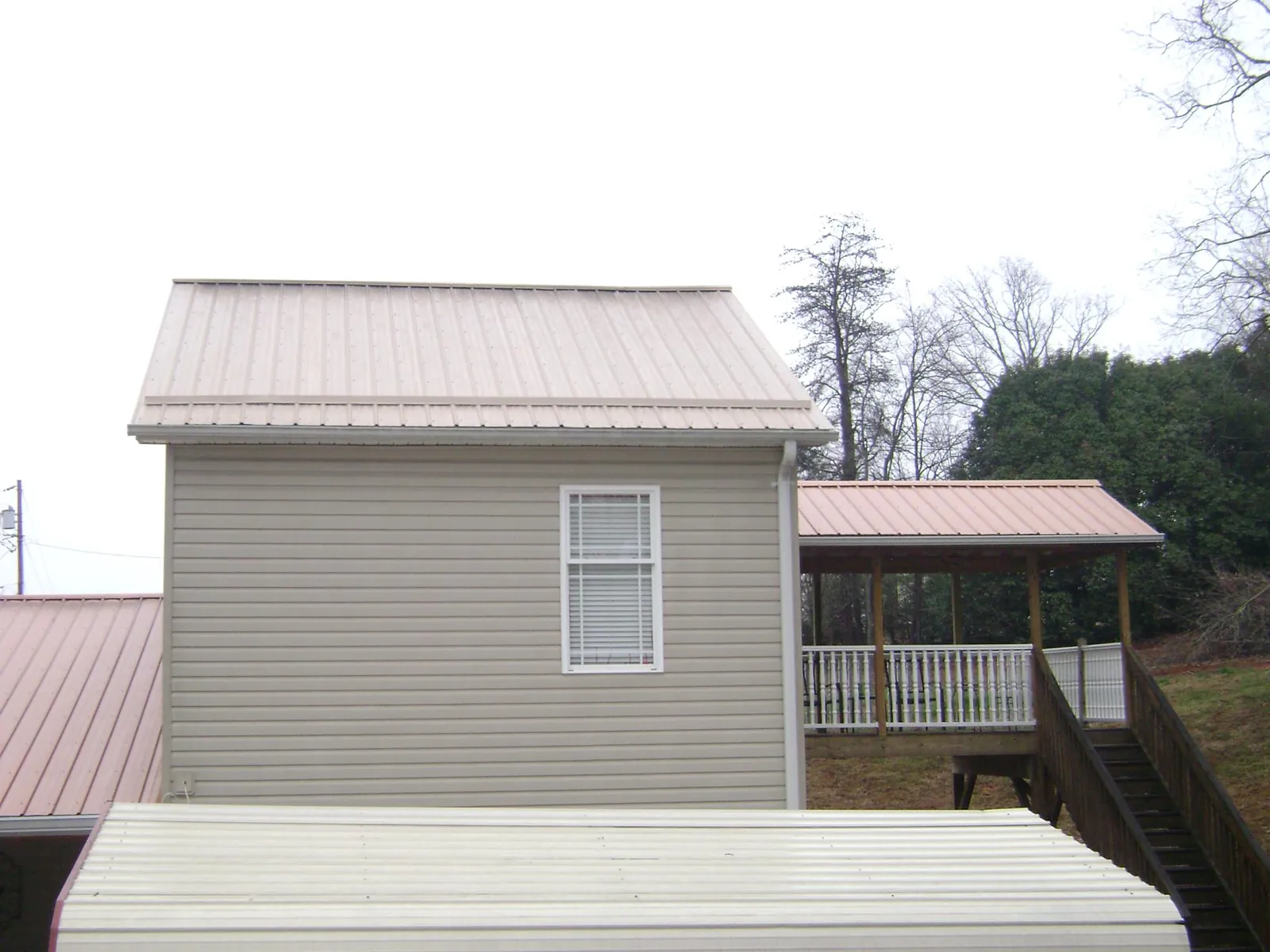 Tan metal roofs on a two story addition and attached porch, from a Roof Replacement job in Vanderbilt