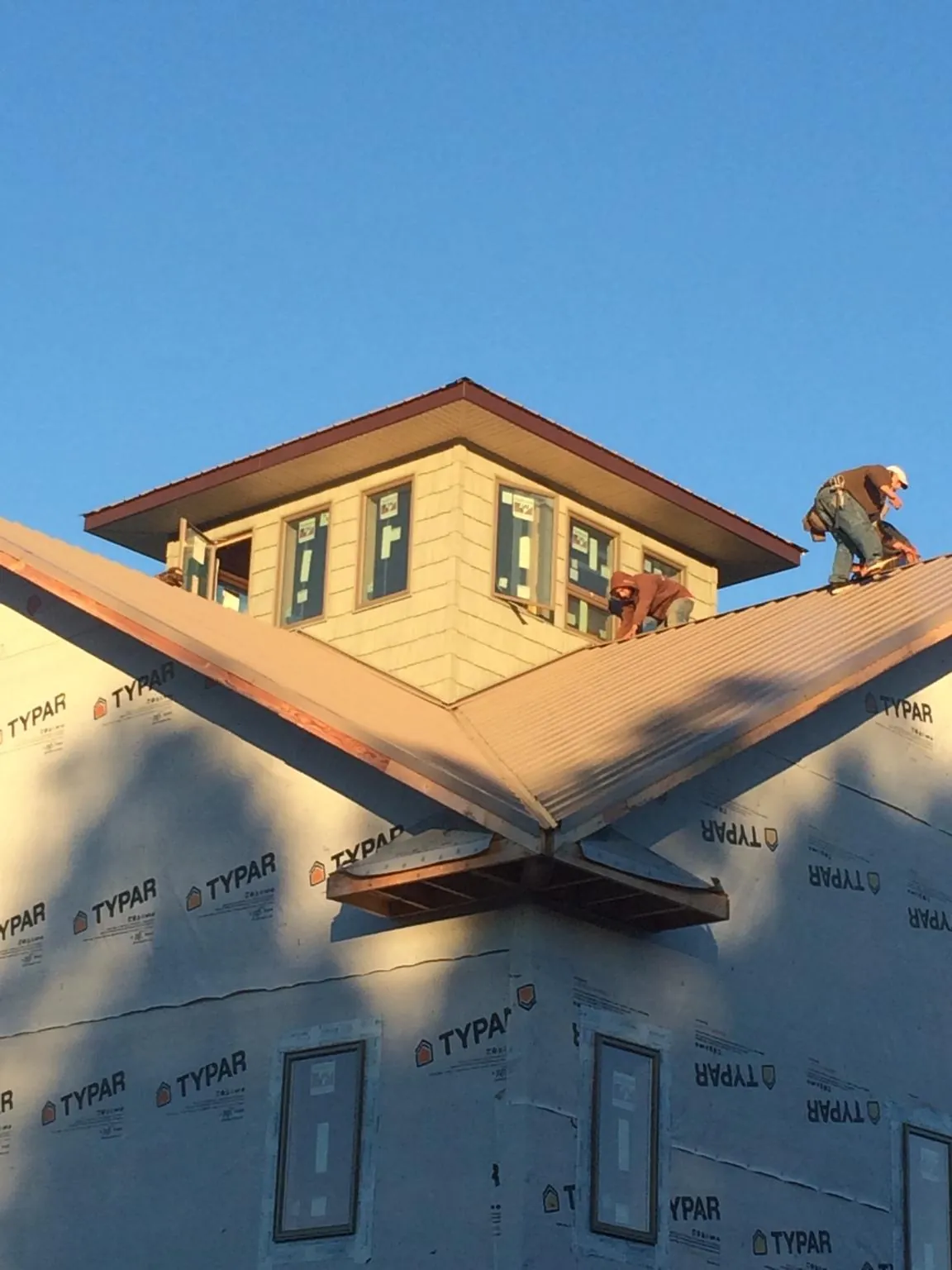 Roofers working around a rooftop cupola on a new metal roof at sunset — Roof Waterproofing in Vanderbilt by Roofing Brothers